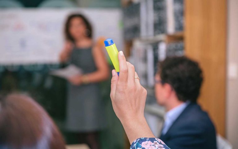 Teilnehmer hebt einen gelben Marker, während eine Dozentin im Hintergrund unterrichtet – Beratung, Führungskräfteschulung und Qualitätskontrolle
