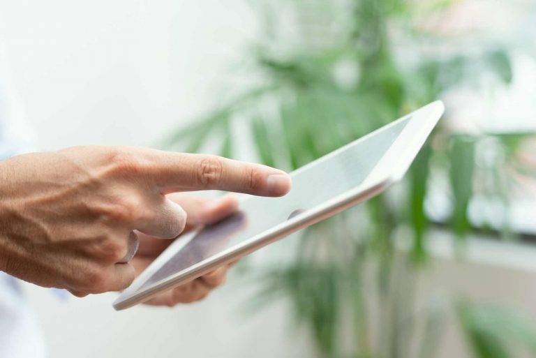 Hand zeigt auf Tablet-Bildschirm mit unscharfem Hintergrund aus Pflanzen – digitale Qualitätssicherung im Fokus