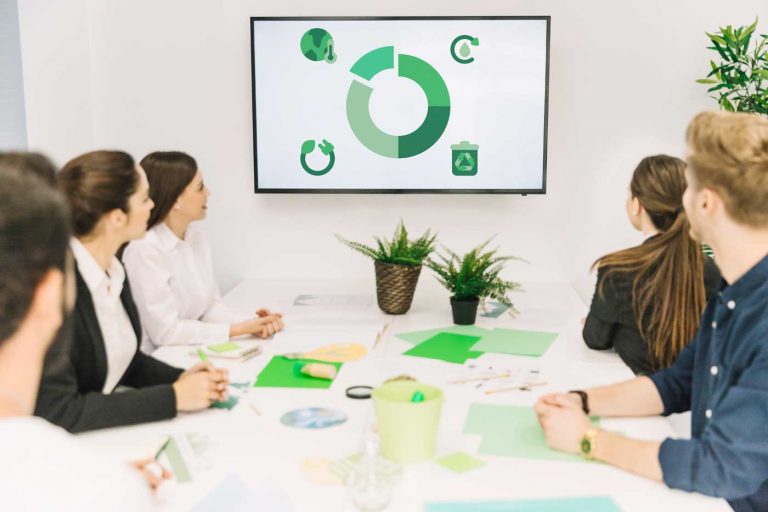 Team sitzt am Konferenztisch und schaut auf einen Bildschirm mit grüner Infografik – nachhaltige Reinigungsprozesse und Seminare