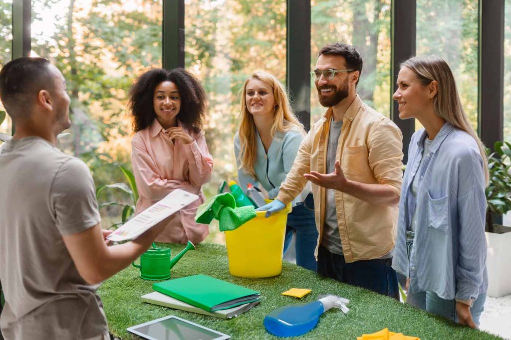 Gruppe von Mitarbeitenden steht um einen gelben Reinigungseimer und diskutiert nachhaltige Reinigungsmaßnahmen – Beratung, Qualitätskontrolle und nachhaltige Reinigung