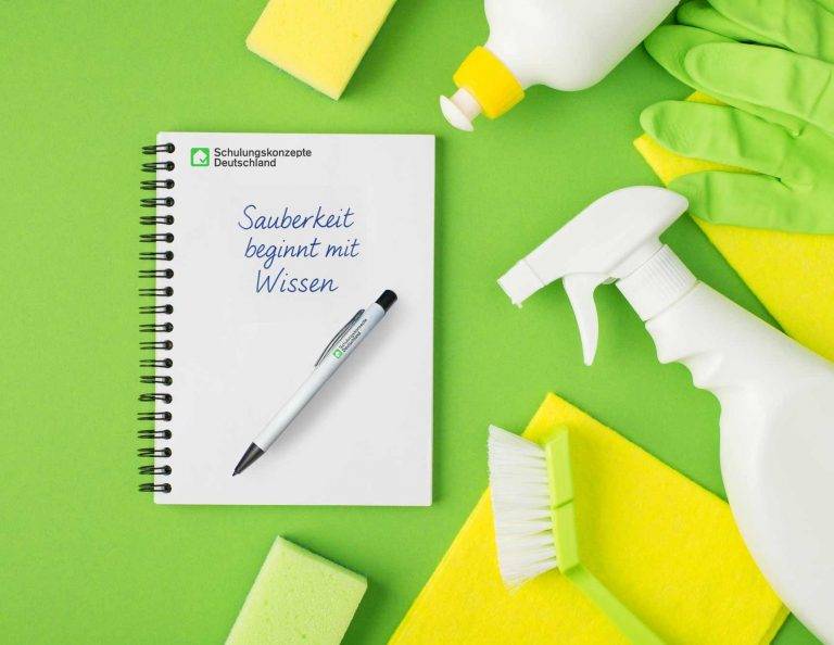 Notizbuch mit dem Slogan 'Sauberkeit beginnt mit Wissen', umgeben von Reinigungsutensilien wie Handschuhen, Schwämmen und Sprühflasche